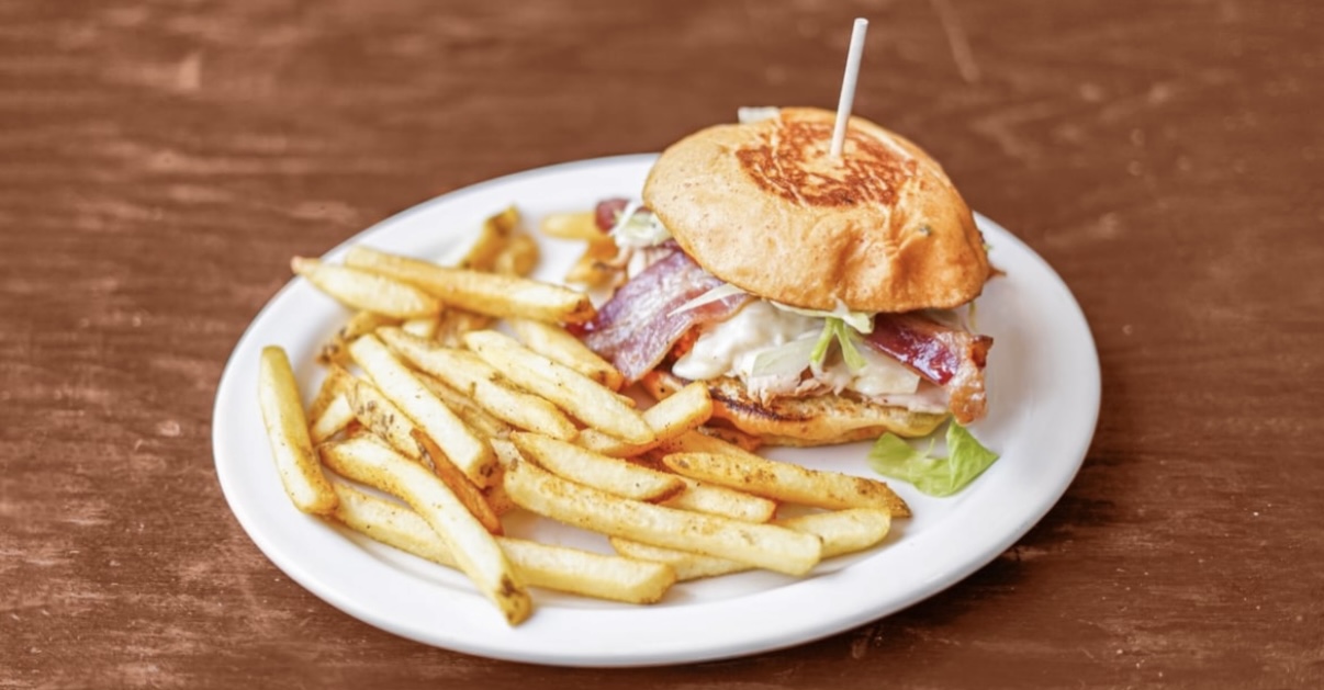 A chicken sandwich with bacon and fries