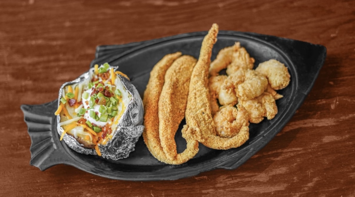 A fish-shaped platter of fried catfish, popcorn shrimp and a loaded baked potato