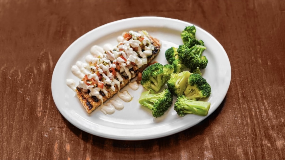 A grilled salmon filet topped with pico de gallo and aioli with steamed broccoli