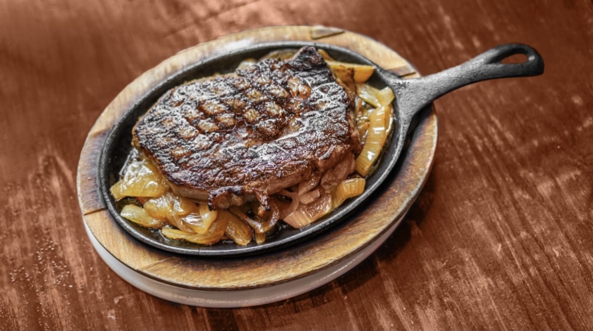 A ribeye sizzling on a cast iron skillet over Cajun onions